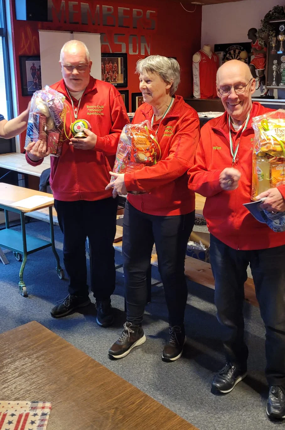 Drie oudere volwassenen in bijpassende rode clubjacks dragen medailles en houden ingepakte geschenkmanden vast.